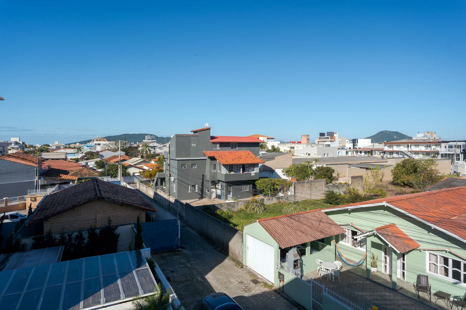 Entorno urbano visto do apartamento, com casas, telhados e morros ao fundo
